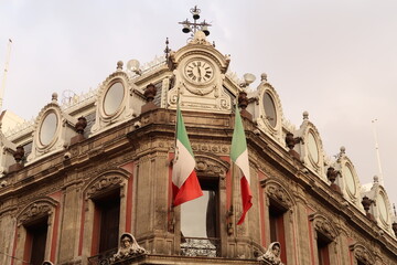 The top of building Edificio La Esmeralda with mexican flags, a clock, and many details and...