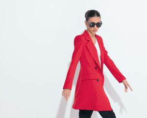 stylish young woman in red coat with sunglasses walking in a cool way