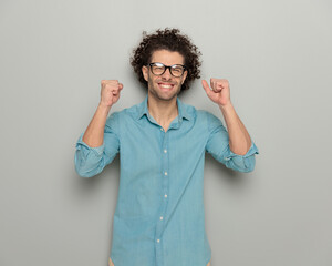 excited casual guy with glasses holding fists up and celebrating victory