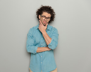 Fototapeta na wymiar thoughtful casual man with curly hair and glasses touching chin and thinking
