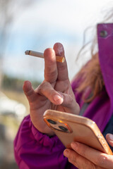 Woman's hand holding a smoking cigarette while using her mobile phone. Concept: vice