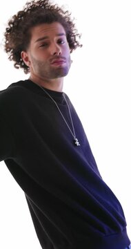vertical video of cool fashion man with curly hair in black hoodie acting innocent, leaning behind and posing in a confident way on grey background