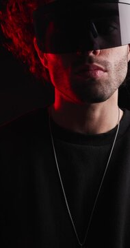 vertical video of casual young man with curly hair adjusting futuristic sunglasses and necklace looking forward on black background