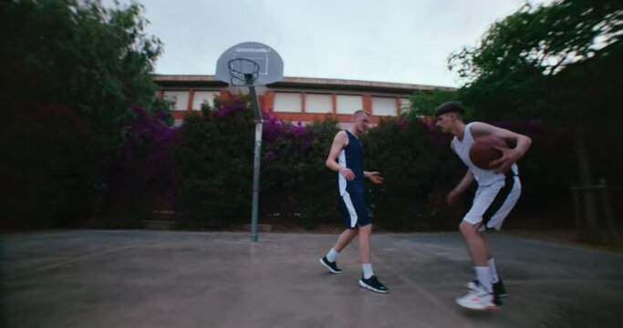Super wide angle shot of two friends or rivals play street basketball outside in park. Urban street sport. Youth free time development program activity. Active and healthy lifestyle