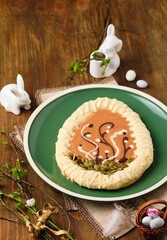 Mazurek, Polish Easter sweet made from shortcrust pastry in the shape of an egg with Easter decoration on a green plate on a wooden background. Polish cuisine.