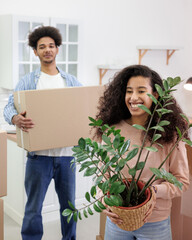 African American couple, man woman, collect clothes and plants in cardboard boxes for moving. happy...