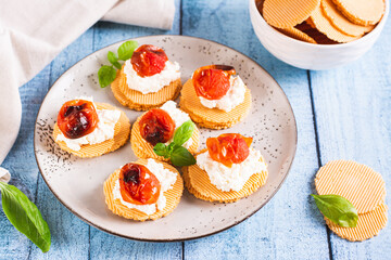 Crostini on crispbread with ricotta, baked tomatoes and basil on a plate