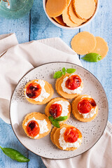 Crostini on crispbread with ricotta, baked tomatoes and basil on a plate top and vertical view