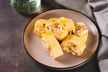 Mini tortilla rolls with chopped sausages, cheese, eggs and herbs on a plate on the table