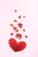 Folded red paper heart and dry flowers on a pink background vertical view
