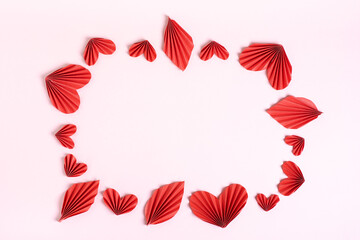 Frame of folded red paper hearts and leaves on pink background top view