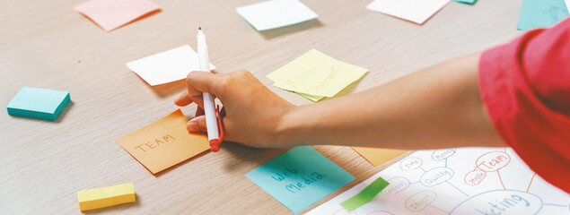 Closeup imaged of young creative businesswoman writes on colorful sticky note and places it on...
