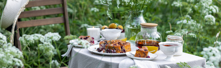 Elegant glamour table setting outdoor in the garden. White porcelain cups, teapot with herbal tea,...