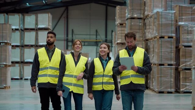 Front view of warehouse workers walking in warehouse. Team of warehouse workers preparing products for shipment.