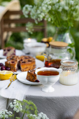 Tea time with sweet homemade cherry cake and herbal beverage in summer garden outdoors. Table covered with linen tablecloth, white porcelain cups. English style