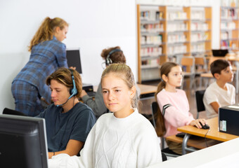 Group of positive teenage boys and girls learning to use computers in classroom