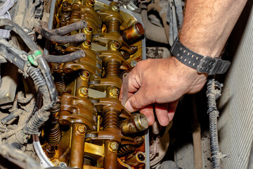Car repairs. An auto mechanic adjusts the thermal clearances of the valves of the gas distribution mechanism with a feeler gauge - obrazy, fototapety, plakaty