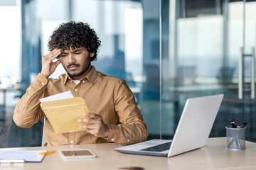 Sad unsatisfied and unhappy business man inside office at workplace, man received mail envelope fox with notification message with bad news, worker reads disappointed.