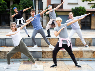 Fototapeta na wymiar Confident teen boys and girls dancing modern choreography on city street on summer day.