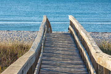 A wide, wooden boardwalk to a beach with a blue ocean.