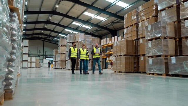 Front view of warehouse workers walking in warehouse. Team of warehouse workers preparing products for shipment.