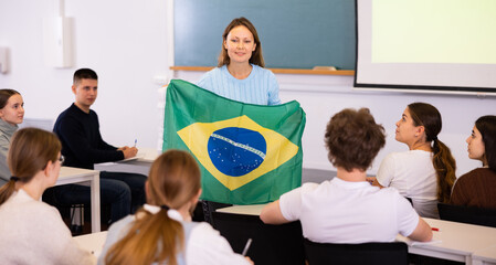 Adult female teacher in the classroom showing the flag of Brazil to the students at the geography...