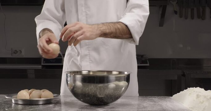 Chef hands break an egg into a bowl. Professional chef prepares dough or dessert