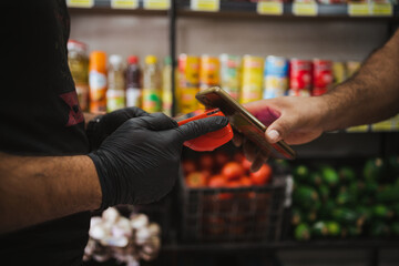 Anonymous man paying on a POS using his phone in a fruit shop in Chile. NFC payment.