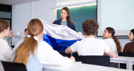 Female teacher tells her classmates about the country of Russian, holding a flag in her hands