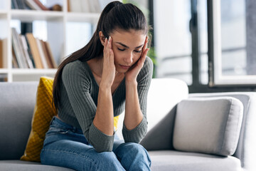 Depressed young woman thinking about her problems while sitting on the sofa at home.