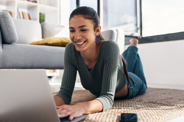 Happy young woman using her laptop while lying on the floor at home