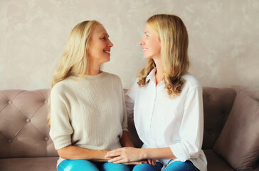Portrait of happy smiling caucasian middle aged mother and adult daughter looking at each other together sitting on couch at home