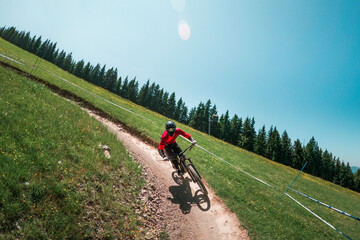 Downhill mountain biking on a shaped bike park trail in Austria, sunny blue sky day, bike leaning in the curve. - 704671822
