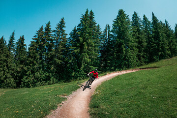 Downhill mountain biking on a shaped bike park trail in Austria, sunny blue sky day, bike leaning in the curve. - 704671824