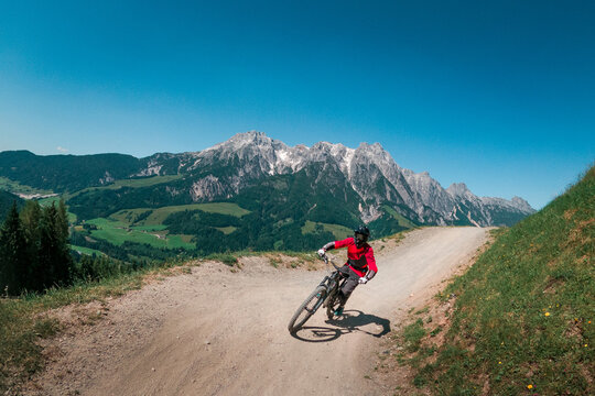 Downhill mountain biking in front of mountain scenery of Wilder Kaiser in the mountains of Austria, sunny blue sky day.