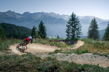Downhill mountain biking on a shaped bike park trail in Austria, sunny blue sky day, trees and mountains in background. - 704672013