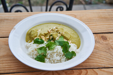 Sweet green curry made from lamb meat, coconut milk, vegetables and sprinkled by cashew nuts with basmati rice in deep vintage plate on wooden table. Delicious and healthy dish from Indian cuisine.