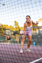 Positive girl in sportswear playing tennis match during training on court. View through tennis net