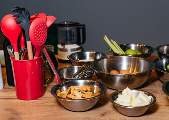 A wooden table with steel bowls containing ingredients for making dessert: ginger cookies, eggs, butter.