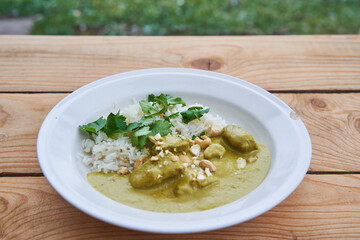 Sweet and spicy lamb curry, traditional recipe from Indian cuisine made from lamb meat, coconut milk, vegetables and cashew nuts with basmati rice and served outdoor in garden on rustic wooden table.