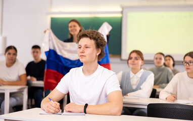 Female teacher tells her classmates about the country of Russian, holding a flag in her hands