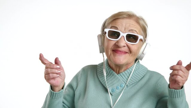 Pretty happy blonde short-haired woman of 60-70 years listening to the music in white headphones, wearing white-rimmed sunglasses, dancing like a youngster. High quality 4k footage