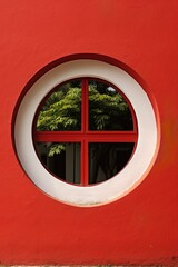 Round window on red wall with green foliage outside
