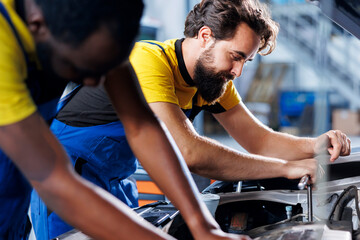 Technicians collaborating on servicing broken vehicle, checking for faulty brakes. Smiling repairmen in auto repair shop working together on fixing automobile, discussing best options - obrazy, fototapety, plakaty