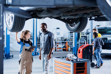 Seasoned mechanic in garage using laptop to follow checklist while doing maintenance on car,...