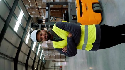 Male warehouse worker standing by forklift. Warehouse manager checking delivery, stock in warehouse, inspecting products for shipment. Vertical view. - Powered by Adobe