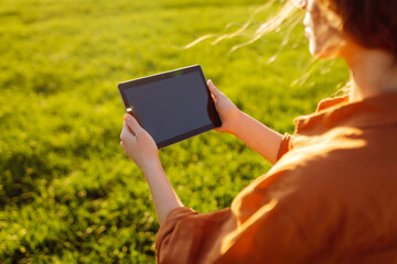 Smart agriculture. A young woman farmer wearing glasses holds a tablet on a green wheat field. A woman agronomist checks the quality of the crop using a digital tablet. Agriculture concept.