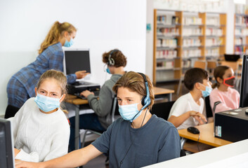 Preteen boy and girl in protective mask learn to solve problems on computer in a school classroom