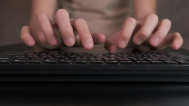 Little arms on computer keyboard indoor. A teenager arms typing something on keyboard on sofa.