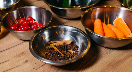 Steel bowls with raw ingredients for cooking at a culinary master class, bowl with cherry tomatoes, peeled carrots, cinnamon sticks and aromatic spices, zucchini and limes
